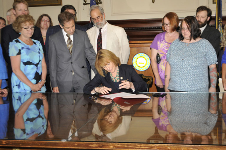 Governor Maggie Hassan signing the Community Mental Health Agreement with stakeholders looking on.