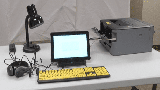 Accessible voting system with headphones, yellow keyboard, tablet, and printer set up on a table