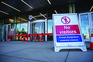 Sign in front of hospital entrance reads No Visitors Except Designated Essential Visitors