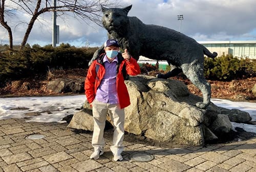 UNH-4U Bridges graduate Garrett Shows standing in front of the UNH wildcat statue giving a thumbs up