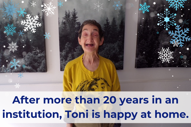 Toni, a woman with disabilities, short dark hair and yellow shirt smiles broadly at the camera. Black and white images of trees are hanging behind her. Text reads 'After more than 20 years in an institution, Toni is happy at home'.