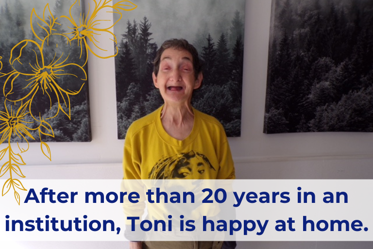 Toni, a woman with disabilities, short dark hair and yellow shirt smiles broadly at the camera. Black and white images of trees are hanging behind her. Text reads 'After more than 20 years in an institution, Toni is happy at home'.